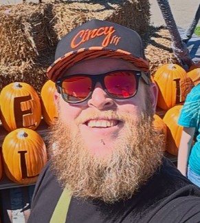 Hatz in a Cincy cap, grinning in front of a wall of painted pumpkins
